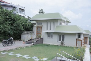 A two-story building with a green roof, a staircase leading to the entrance, and a motorcycle parked in front.