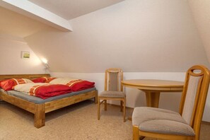 A bedroom with a wooden bed, a small table, two chairs, and a wall-mounted light. - Holiday apartment with 2 bedrooms (Haide\/Ummanz)