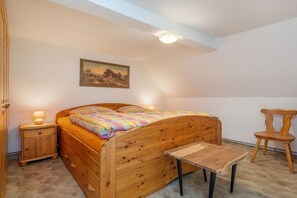Une chambre à coucher avec un lit en bois, une table de chevet, une chaise en bois et un tableau accroché au mur.