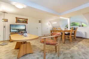 Un coin repas avec une table ronde en bois, des chaises, un téléviseur et un tableau accroché au mur.