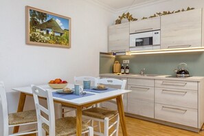 A compact kitchen with a microwave, sink, and cabinets. There is a dining table with chairs and a bowl of fruit. - "Nymph" in the Villa Frigga (Binz)