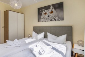 A hotel room with a bed, pillows, a headboard, a wall-mounted painting of an owl, a wardrobe, and a bedside table with a lamp. - 13, Residence Dünenstraße (Binz)
