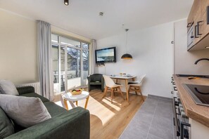 A modern living room with a sofa, a dining area with a table and chairs, a kitchen with a stove, and a TV mounted on the wall. - 13, Residence Dünenstraße (Binz)