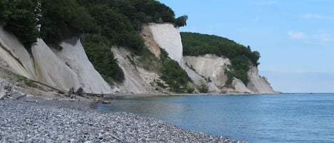 Une plage de galets, avec une falaise rocheuse et un ciel dégagé.