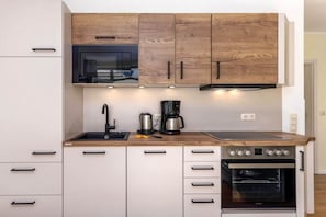 A modern kitchen with wooden cabinets, a built-in oven, and a coffee maker. - 13, Residence Dünenstraße (Binz)