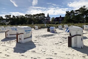 Strandstühle und Sonnenschirme am sandigen Strand, im Hintergrund eine Kirche und Häuser.