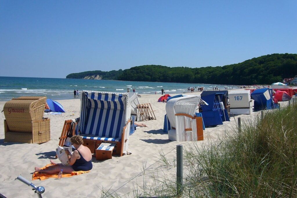 A beach with beach chairs and umbrellas, a beachside café, and a view of the sea and hills.