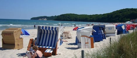 A beach with beach chairs and umbrellas, a beachside café, and a view of the sea and hills.