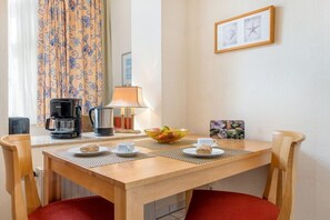 A hotel room with a wooden table set for breakfast, a coffee maker, a lamp, and a framed picture on the wall. - Starfish in Villa Lucky (Binz)