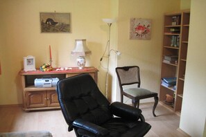 A living room with a black leather chair, a wooden bookshelf, a lamp, and a painting on the wall. - Hof Freitag Geestequelle (Hipstedt)