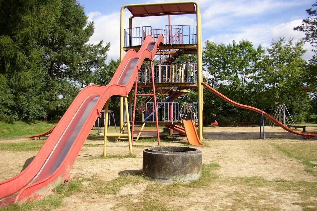 A playground with a red slide, a yellow climbing structure, and a circular concrete feature.