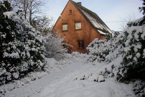 A brick house with a sloped roof surrounded by snow-covered trees and bushes. - Hof Freitag Geestequelle (Hipstedt)