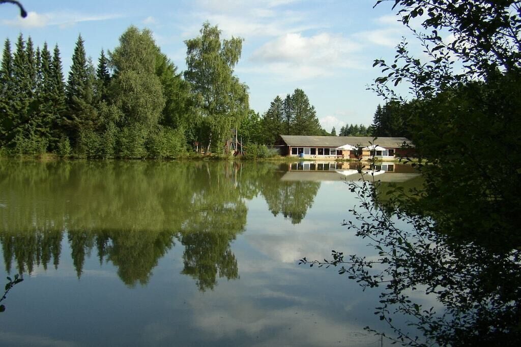 A lakeside cabin with a reflection in the water, surrounded by trees.