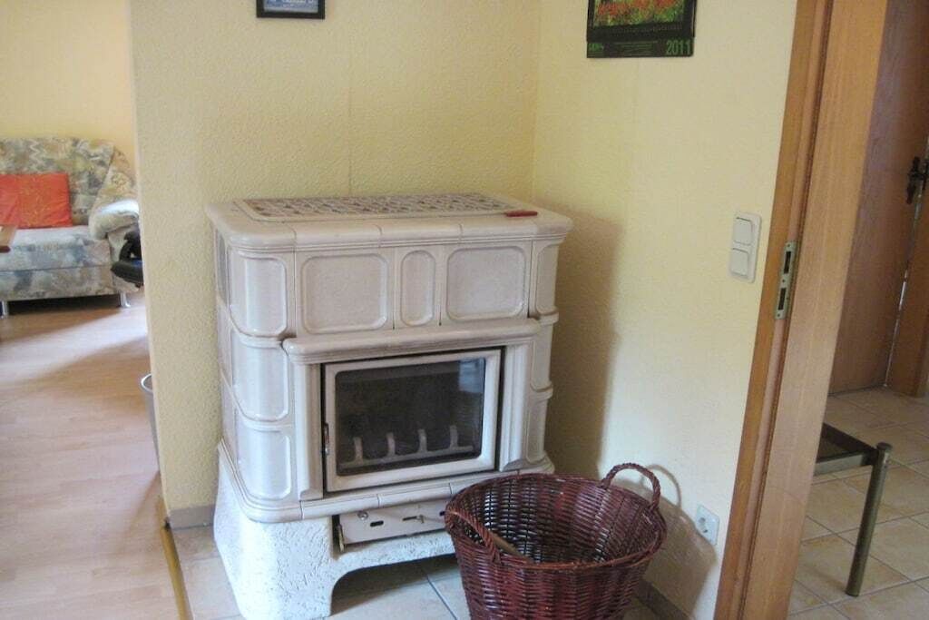 A room with a white fireplace, a wicker basket, and a couch with a red cushion.