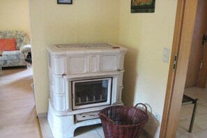 Una habitación con chimenea blanca, una cesta de mimbre y un sofá con un cojín rojo.