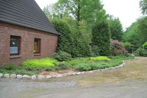 A brick building with a sloped roof, surrounded by a well-maintained garden with various shrubs and a stone border. - Hof Freitag Geestequelle (Hipstedt)