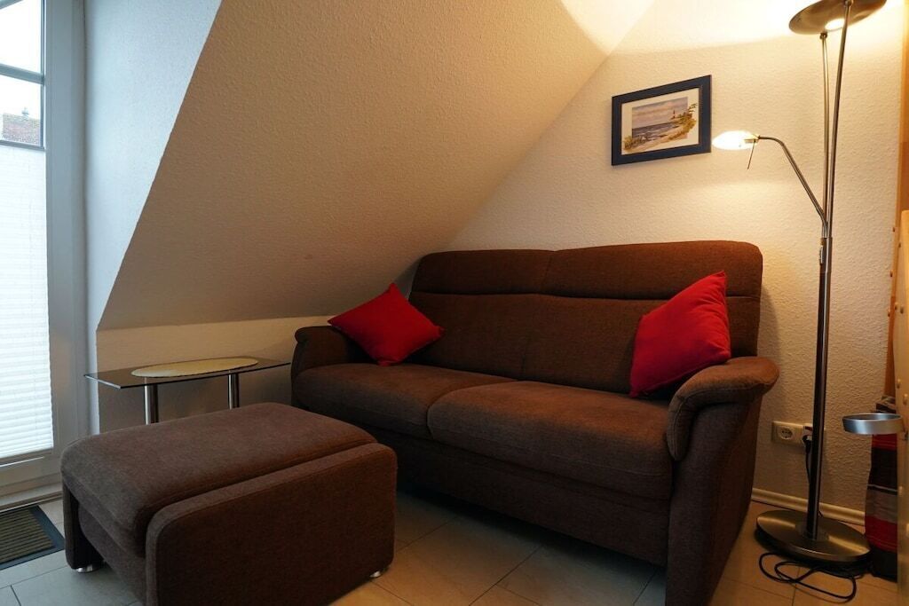 A cozy living area with a brown sofa, two red cushions, a small round table, and a floor lamp.