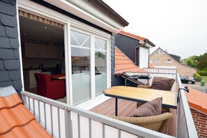 Ein Balkon mit Tisch und Stühlen, eine Glastür zum Küchenbereich und ein Backsteinhaus im Hintergrund.