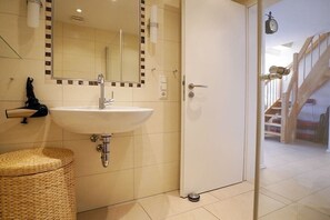 A bathroom with a white sink, a mirror, and a door leading to a staircase. - Holiday apartment with 1 bedroom (Norden-Norddeich)