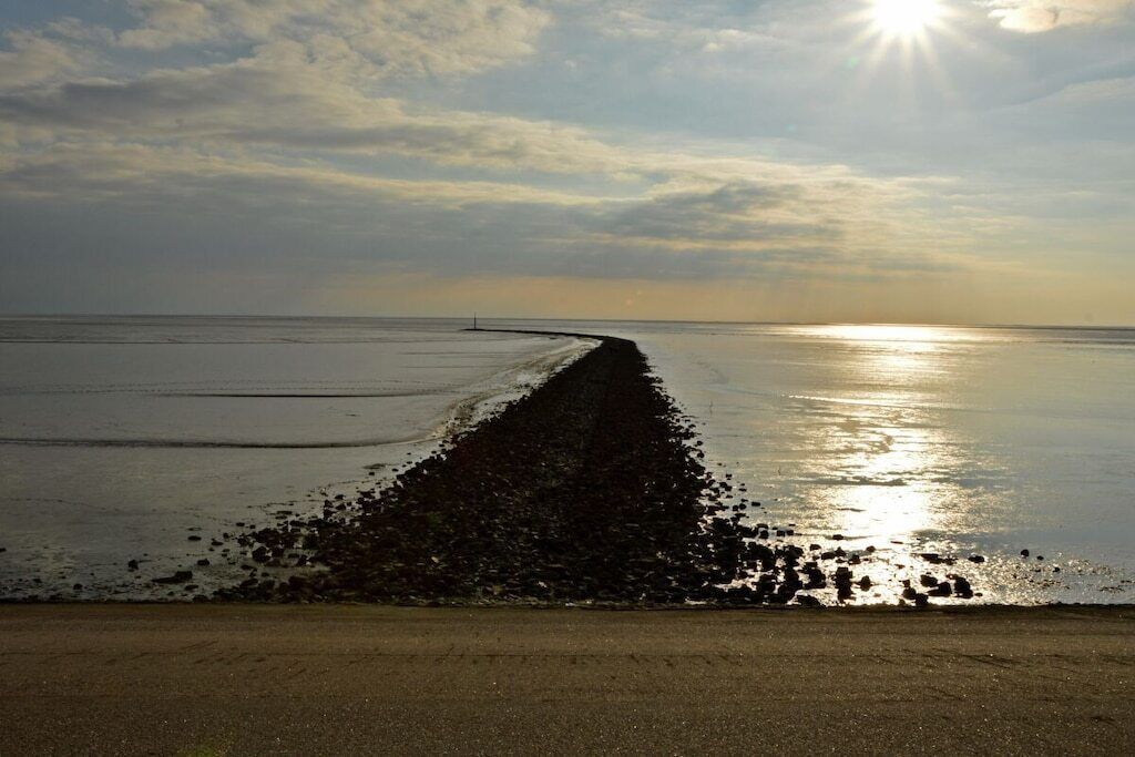 A beach with a long, narrow path leading to the water, a clear sky, and the sun low on the horizon.