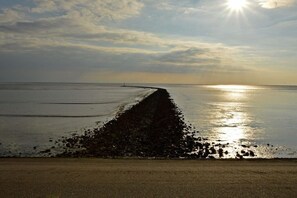 Ein Strand mit einem langen, schmalen Pfad zum Wasser, blauem Himmel und tiefstehender Sonne.