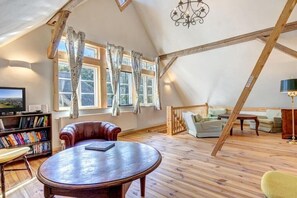 A loft-style room with a wooden floor, a round table, a leather armchair, a sofa, a bookshelf, and a television. - Garden house by the swan pond (Lassan)