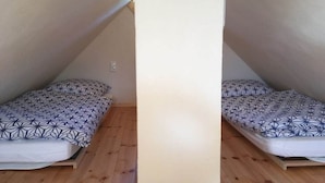 A small, single-occupancy room with a sloped ceiling, wooden flooring, and a bed with a geometric-patterned bedspread.