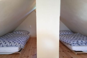 A small, single-occupancy room with a sloped ceiling, wooden flooring, and a bed with a geometric-patterned bedspread.