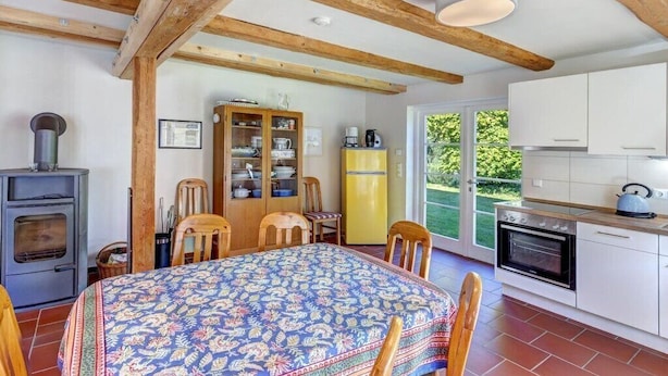 A kitchen with wooden beams, a dining table with chairs, a stove, and a refrigerator.