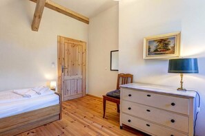 Habitació amb un llit, un taulell, una cadira, una porta de fusta i una làmpada penjada a la paret.