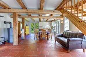 A spacious living area with a fireplace, a dining table with chairs, a leather sofa, and a staircase. - Garden house by the swan pond (Lassan)