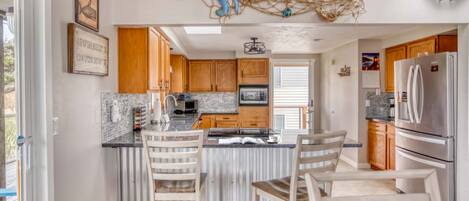 A modern kitchen with wooden cabinets, a marble countertop, and a large refrigerator.