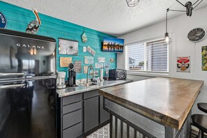 Eine Küche mit einem schwarzen Galanz-Kühlschrank, einer Kaffeemaschine und einem Toaster. An der Wand befinden sich mehrere Nummernschilder, ein Fernseher und eine Uhr.