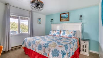 Una camera da letto con un letto, un comodino, una finestra con tende, una ventola a soffitto e un quadro appeso al muro.