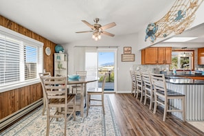 A modern kitchen with wooden cabinetry, a dining area with a table and chairs, and a view through the glass door. - Lincoln City Amazing View Retreat: Hot Tub, Arcade Room, Steps to Beach (Lincoln City)