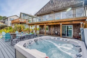 A hot tub on a wooden deck with outdoor furniture, a covered patio area, and a house with a balcony. - Lincoln City Amazing View Retreat: Hot Tub, Arcade Room, Steps to Beach (Lincoln City)
