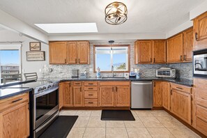 Eine moderne Küche mit Holzausstattung, Backofen, Geschirrspüler und einem großen Fenster mit Aussicht.