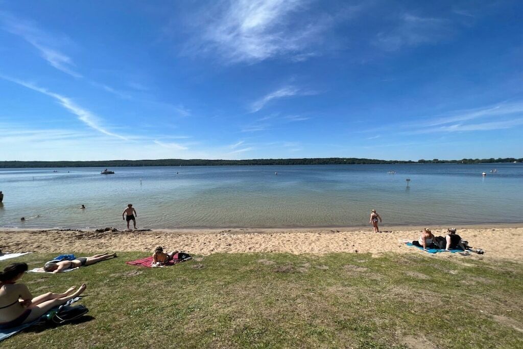 A beach with people sunbathing and swimming, a boat in the water, and a clear sky.