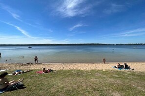 A beach with people sunbathing and swimming, a boat in the water, and a clear sky. - Holiday apartment with 1 bedroom (Neubrandeburg)