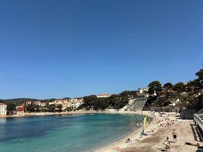 A coastal beach scene with clear blue waters, a sandy shore, and buildings in the background. - Apartment L’Azur Bandolaise by Sur la mer (Bandol)