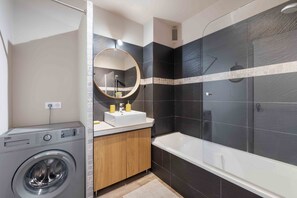 A modern bathroom with a washing machine, a sink with two soap dispensers, a mirror, and a bathtub. - Apartment L’Azur Bandolaise by Sur la mer (Bandol)
