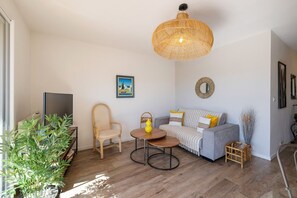 A living room with a sofa, a chair, a coffee table, a television, and a hanging light fixture. - Apartment L’Azur Bandolaise by Sur la mer (Bandol)