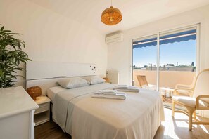 A bedroom with a bed, bedside table, lamp, and a view of the outside. - Apartment L’Azur Bandolaise by Sur la mer (Bandol)