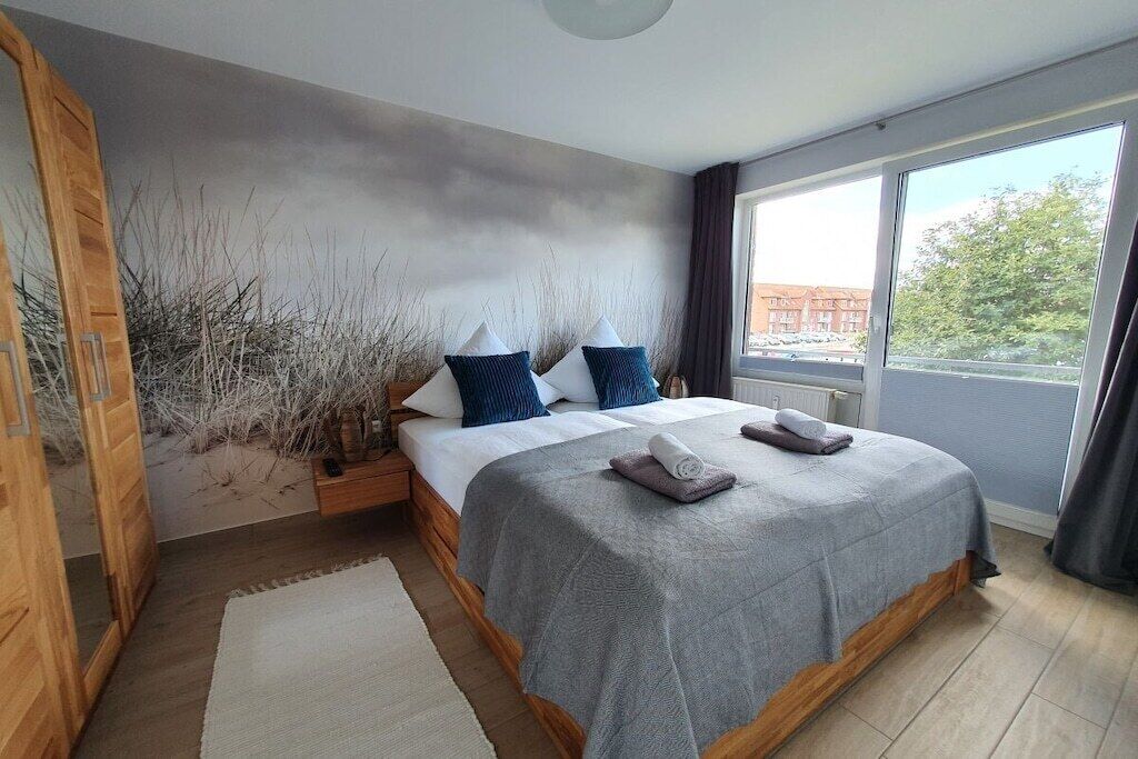 Quarto com cama, mesa de cabeceira, janela e vista para o exterior.