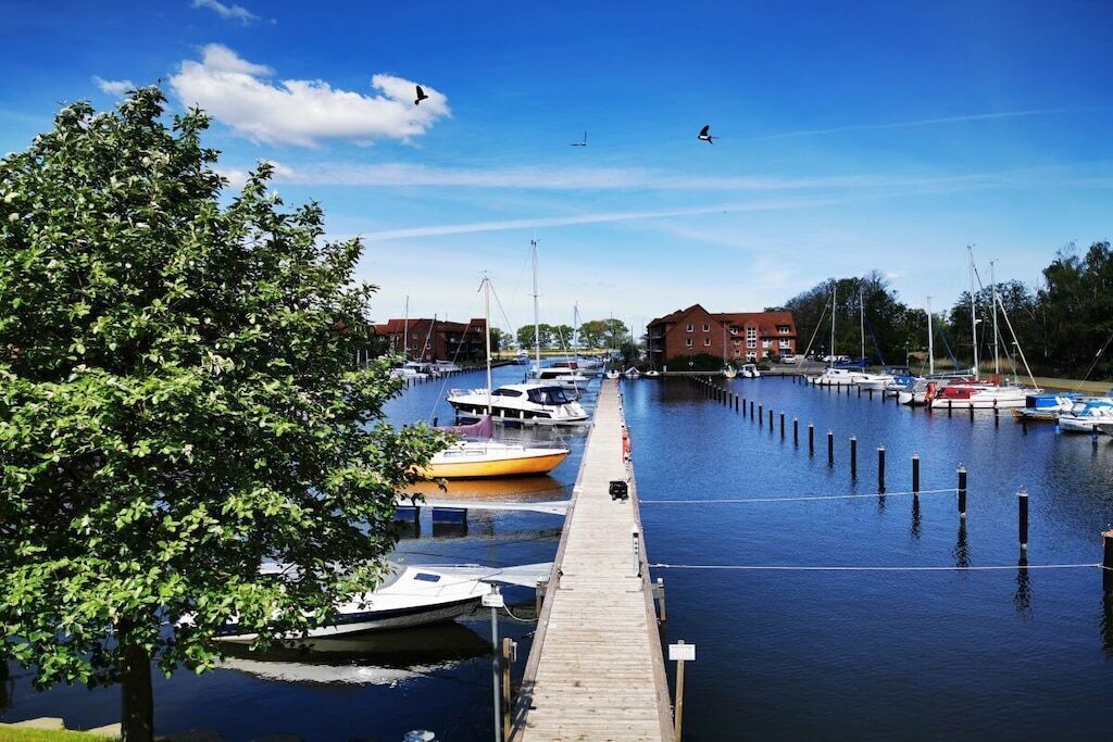 A marina with boats docked, a wooden pier, and buildings in the background.