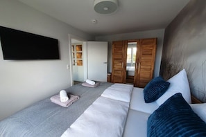 Ein Schlafzimmer mit einem Bett, einem Flachbildfernseher, einem Kleiderschrank und einer Tür zu einem weiteren Raum.