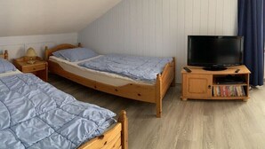 Quarto com duas camas de solteiro, uma televisão sobre um suporte de madeira e uma estante de livros.