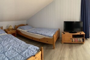 Un dormitorio con dos camas individuales, un televisor sobre un soporte de madera y una estantería.
