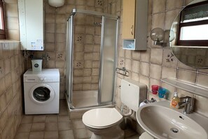 Un baño con lavadora, cabina de ducha, inodoro y lavamanos.