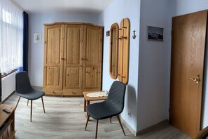 Une pièce avec une armoire en bois, deux chaises, une petite table et une porte.
